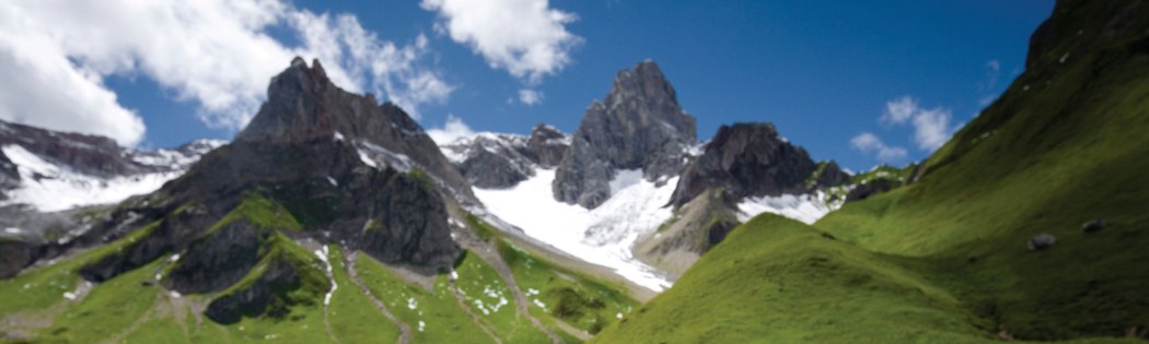 A scene in the Alps, with rocky peaks, snow and green meadows