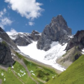 A scene in the Alps, with rocky peaks, snow and green meadows