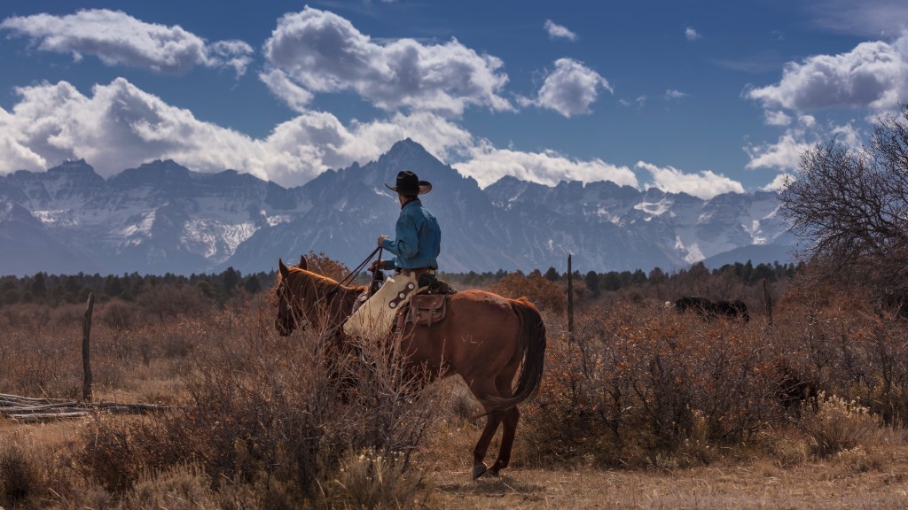 A cowboy riding a horse in a landscape with mountains in the background and scattered clouds in the sky.