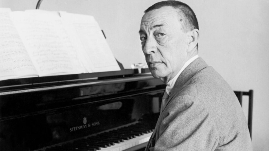 A black and white portrait of a pianist sitting at a Steinway piano, with sheet music visible on the stand.
